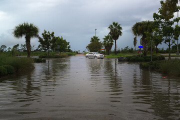 vehicle driving in parking lot submerged under heavy rain, with water pooling  creating  stormy scene.