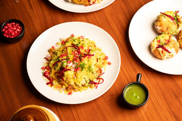 Indian chaat bhelpuri garnished with anardana seeds, served alongside gol gappe and green chutney in a white plate, all arranged on a rustic brown table for a vibrant street food scene. © Lucky Tony 
