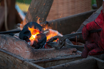a blacksmith heats a workpiece in a furnace, holding it with tongs