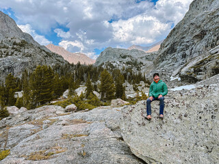 Fototapeta premium A young man sits on a rock in the Wind River Range of Wyoming.