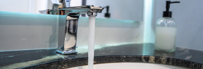 The water is running from the faucet in the bathroom. Waste of water, ecological concept