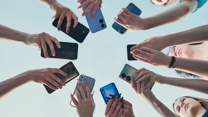 Group of friends holding smartphones making a circle with mobile phones in the sky.