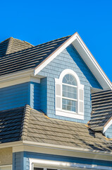 Top of grey stucco luxury house with shingle roof, red and yellow trees and nice windows in Summer in Vancouver, Canada, North America. Day time on June 2024.