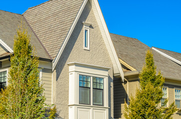 Obraz premium Top of grey stucco luxury house with shingle roof, red and yellow trees and nice windows in Summer in Vancouver, Canada, North America. Day time on June 2024.