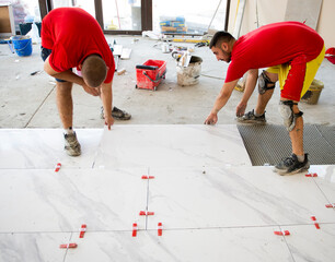 Two young ceramicists are laying ceramic floor tilesve with a tile leveling system