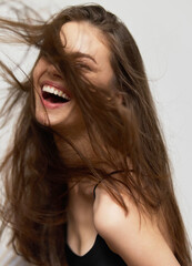 Smiling young woman with long hair playfully tossing her hair, showcasing joy and spontaneity...