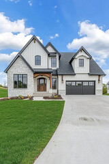 Modern farmhouse style home with stone exterior, black shingle roof, and dark grey accents. Large front porch. White walls, wood beams on the gable sides. Black garage door.