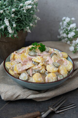 angerichteter Kartoffelsalat auf Tisch aus Holz mit Tuch und Blumen