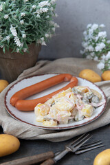 angerichteter Kartoffelsalat mit Wiener Würstchen auf Tisch aus Holz mit Tuch und Blumen