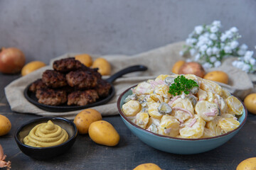 angerichteter Kartoffelsalat mit Frikadellen auf Tisch aus Holz mit Tuch und Blumen