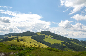 Beautiful mountain landscape showcasing rolling hills and dense forests under a partly cloudy sky....