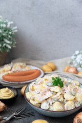 angerichteter Kartoffelsalat mit Wiener Würstchen auf Tisch aus Holz mit Tuch und Blumen