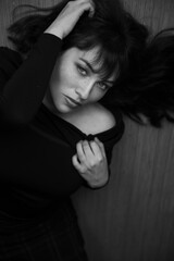 Obraz premium Black and white portrait of a woman laying on a wooden floor wearing a black shirt. This is a close up portrait. She has long dark hair with bangs.