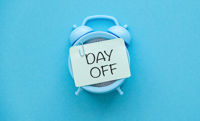Business Day Off Annual Leave, Relaxation, Holiday or Vacation Concept. Blue alarm clock with a note paper on blue background with the message day off