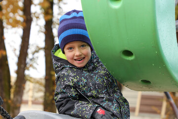 In the fall, a little boy climbed onto a swing at a playground and showed his teeth, smiling.