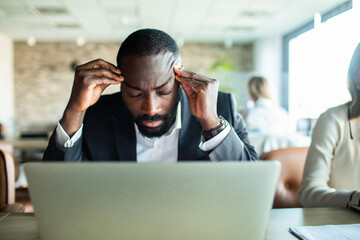 Stressed businessman working on laptop in office setting