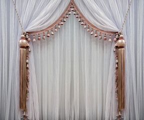 Elegant curtains in a classic style made of white translucent tulle, decorated with luxurious, large tassels
