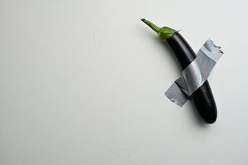 Eggplant Taped to Wall Minimalist Art. A glossy purple eggplant attached to a white wall with duct...