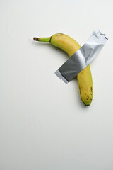 A ripe yellow banana taped to a white wall with duct tape, illustrating a playful and thought-provoking art concept.
