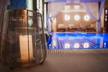 A luxurious indoor pool area features a decorative lantern with a lit candle, vibrant blue...