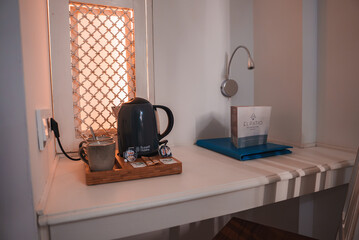 A cozy room corner features a dark electric kettle, cup, and sachets on a tray. A lattice window and modern lamp enhance the traditional contemporary decor.