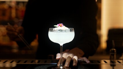 Bartender serving mixed creamy vodka cocktail glass adding pink flower top with sugar burned on ice at bar, focusing alcohol refreshing special created menu at luxurious counter nightclub. Vinosity.
