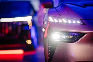 Close-up of two modern cars with illuminated LED headlights, bokeh effects, and vibrant purple and...