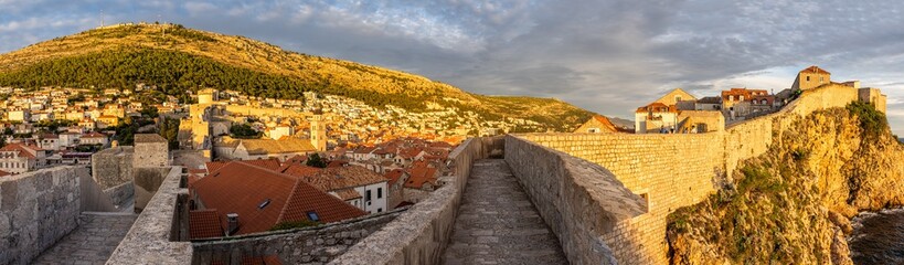Panoramic photo of Dubrovnik from the city walls. Highlights include red and orange tiled roofs, vibrant blue sea and medieval architecture. Dubrovnik, Croatia