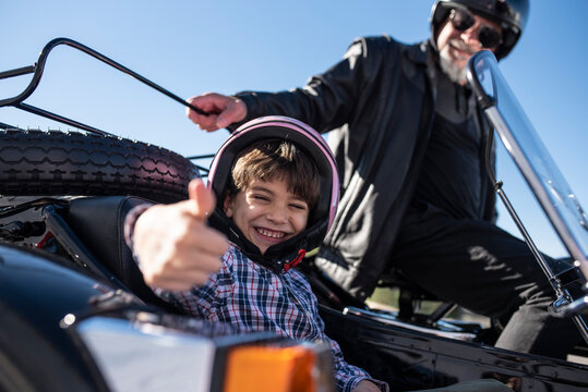 little boy makes the ok sign to the camera while riding in his grandfather's sidecar