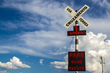 Old railway crossing sign with the warning to stop, look, listen in portuguese, from the deactivated railway with cluody ble sky background in Brazil