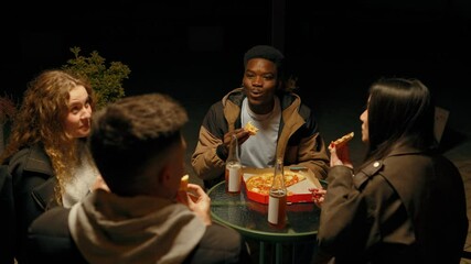 Friends enjoy late-night pizza and drinks outdoors at a lively gathering on a warm evening