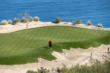 overview of man in red shirt on the edge of putting green with water in  the background