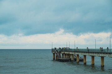 Obraz premium People Walking on a Pier Overlooking the Ocean at Dusk With Dramatic Clouds Above