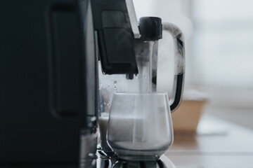 A modern coffee machine brewing a hot beverage in a glass cup, emitting steam in an office kitchen. The image captures a moment of relaxation and efficiency.