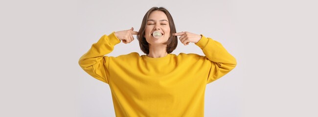Funny young woman with chewing gum on light background