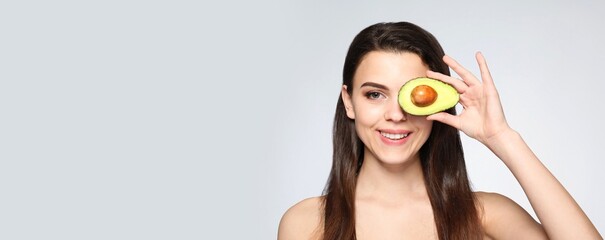 Beautiful naked young woman with avocado on light background with space for text