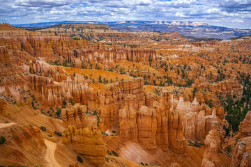 Stunning view of Bryce Canyon National Park featuring unique rock formations and natural amphitheaters. A breathtaking landscape of orange and red rocks combined with a blue sky and dramatic clouds.  © Don