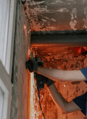 Young caucasian builder carpenter holds an angle grinder in his hands and cuts a stud from a wall