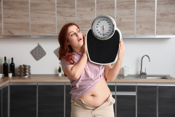 Young overweight woman with scales wearing tight pants in kitchen