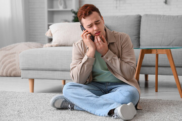 Young man talking with mobile phone and suffering from toothache in room