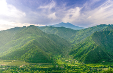 Fototapeta premium amazing view at a green landscape between two mountains with a high peak with snow and blue cloudy sky on background