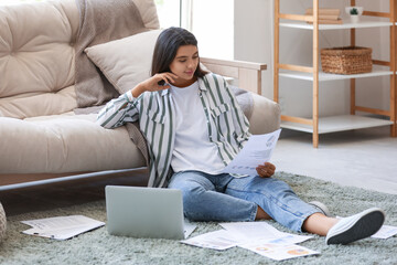 Young beautiful businesswoman sitting on floor with documents near laptop in home office