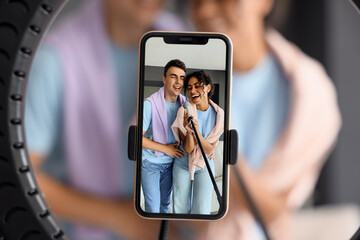 Young bloggers with microphone recording video on screen of mobile phone at home, closeup