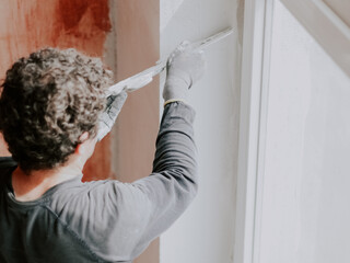 A Caucasian young man is putting putty on the wall.