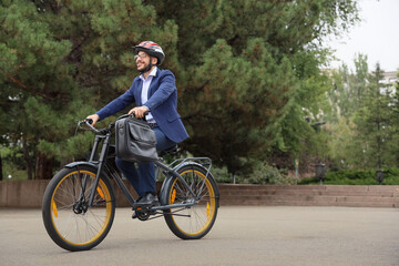 Young happy businessman in helmet with briefcase riding bicycle on city street