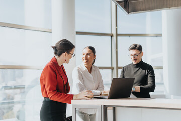 A group of business employees are gathered in an office kitchen, engaged in a collaborative...