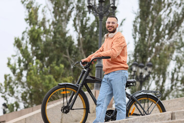 Fototapeta premium Young happy man with headphones and bicycle going downstairs in city