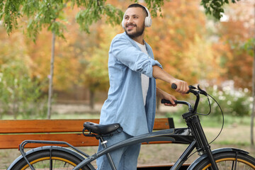 Obraz premium Young happy man in headphones with bicycle at park on autumn day