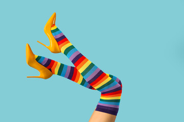 Legs of young woman in colorful stockings and yellow high heels on blue background