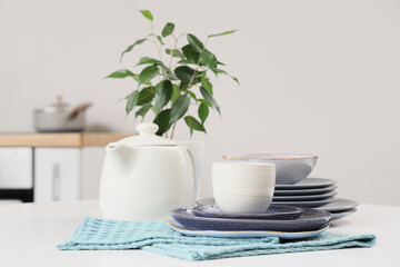 Different clean dishes and teapot on white table in kitchen